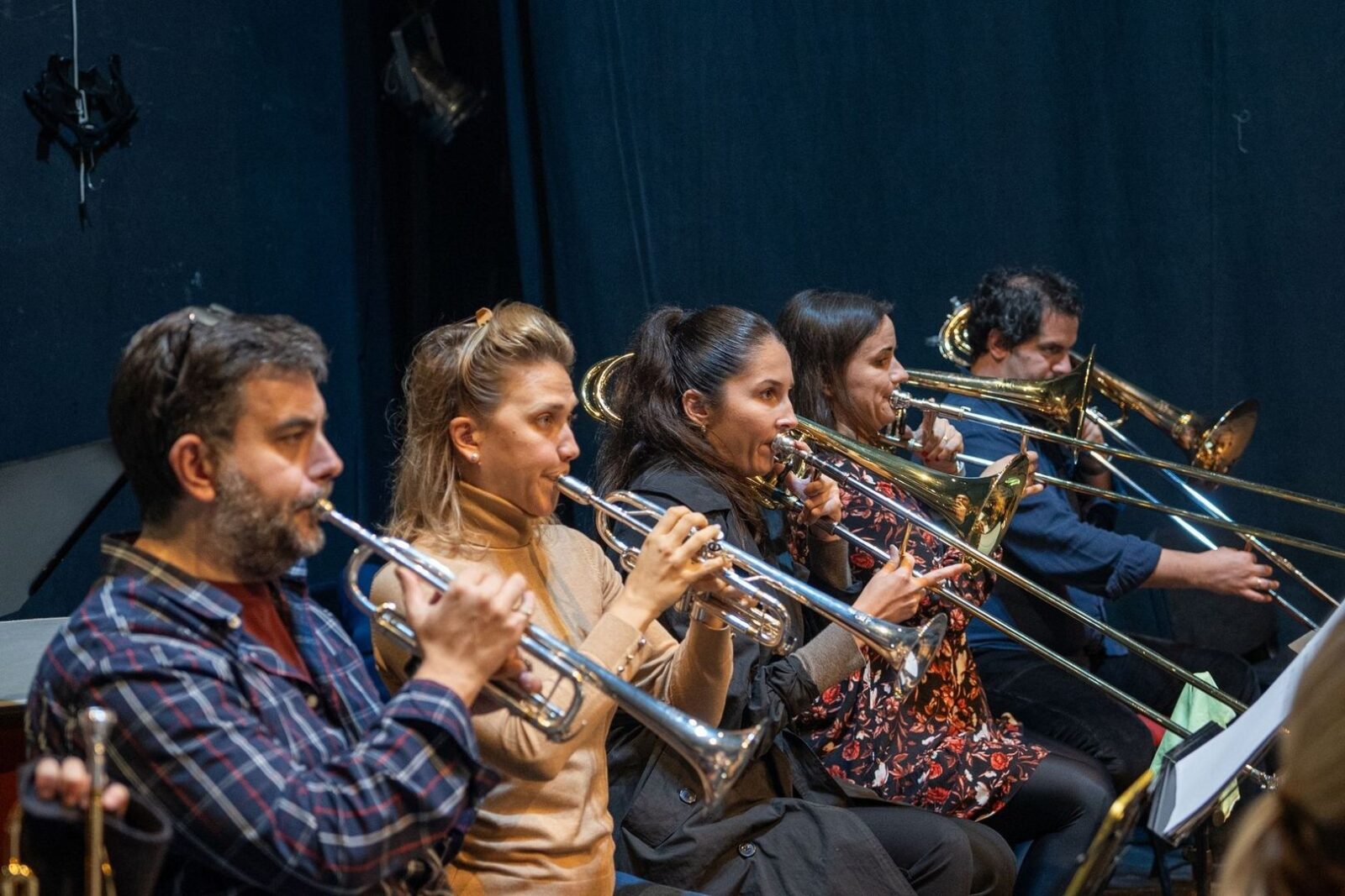 Brass musicians rehearse together in a dark music room