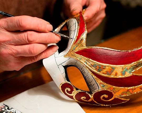 Hands use tools to detail a colorful handcrafted carnival mask