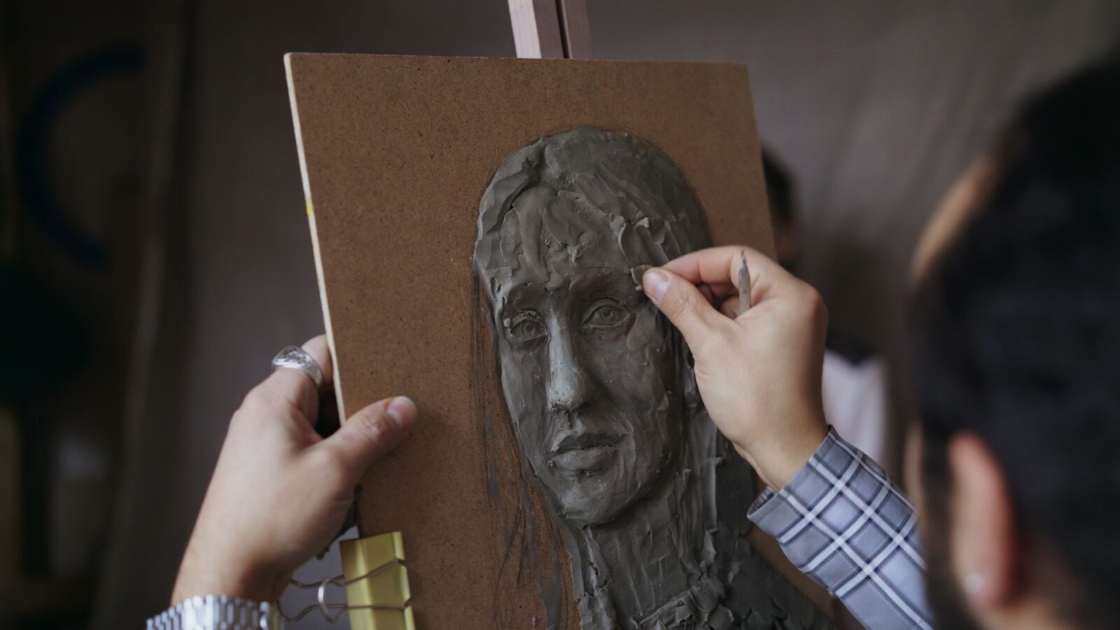 Craftsperson shaping a clay face mask model with a sculpting tool